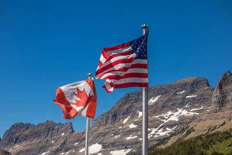 Photo of the Canadian and American flags in front of a mountain.